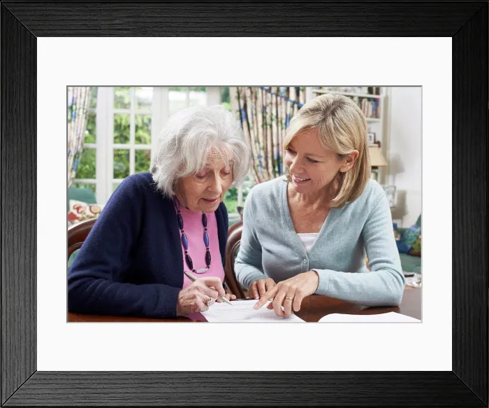 Framed Print : Female Neighbor Helping Senior Woman To Complete Form Framed Print : Female Neighbor Helping Senior Woman To Complete Form