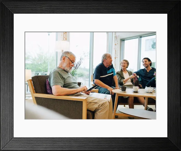 Framed Print : Senior man using smart phone while sitting with newspaper on armchair by friends and caretaker at elderly nursing home Framed Print : Senior man using smart phone while sitting with newspaper on armchair by friends and caretaker at elderly nursing home