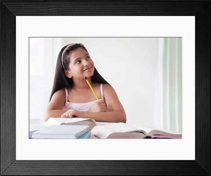 Framed Print : Portrait of smiling cute girl thinking at desk with books Framed Print : Portrait of smiling cute girl thinking at desk with books