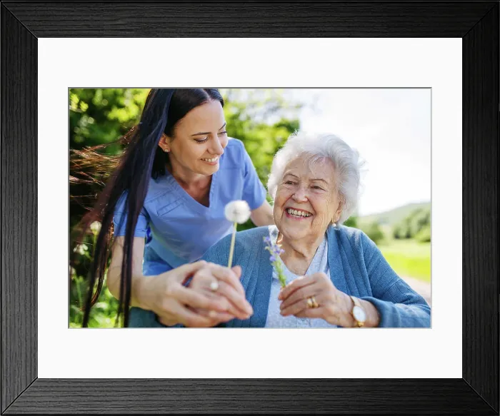 Framed Print : Female caregiver and senior woman in wheelchair holding dandelion