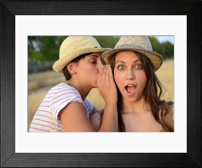 Framed Print : Young woman whispers in friends ear Framed Print : Young woman whispers in friends ear
