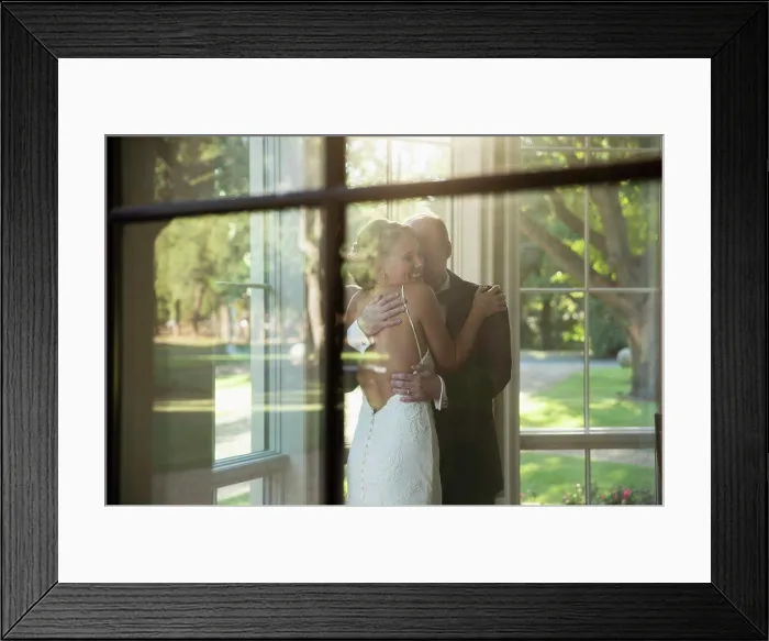 Framed Print : Bride and father of the bride embracing celebrating the wedding day, seen through window Framed Print : Bride and father of the bride embracing celebrating the wedding day, seen through window