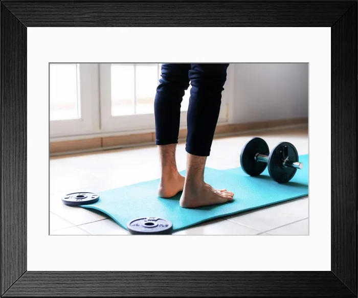 Framed Print : Low angle back view of crop barefooted male athlete in sportswear standing on bright blue sports mat against black