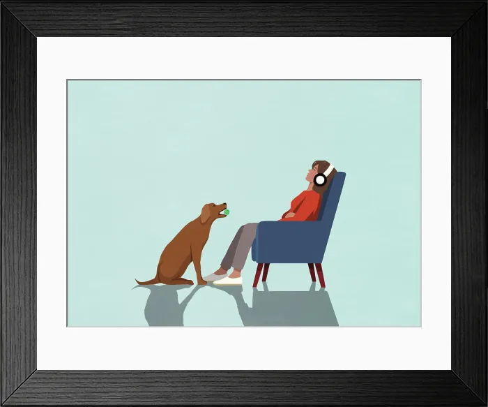 Framed Print : Dog with ball sitting in front of oblivious woman with headphones in armchair