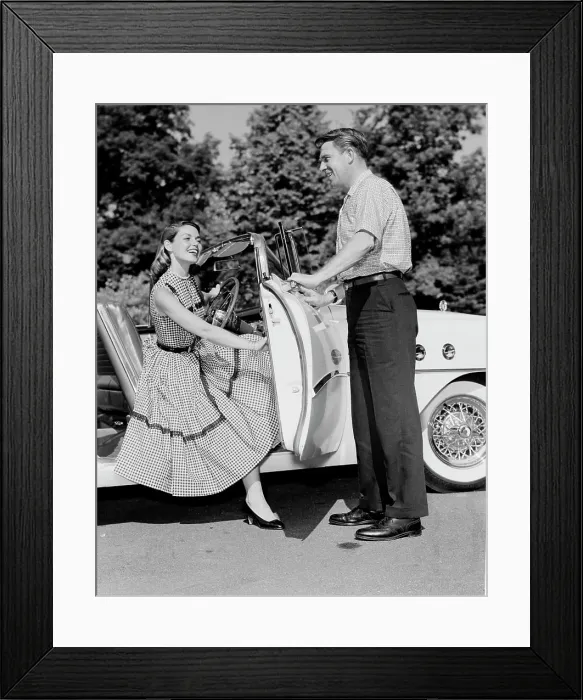 Framed Print : Young woman getting of convertible, young man opening car door