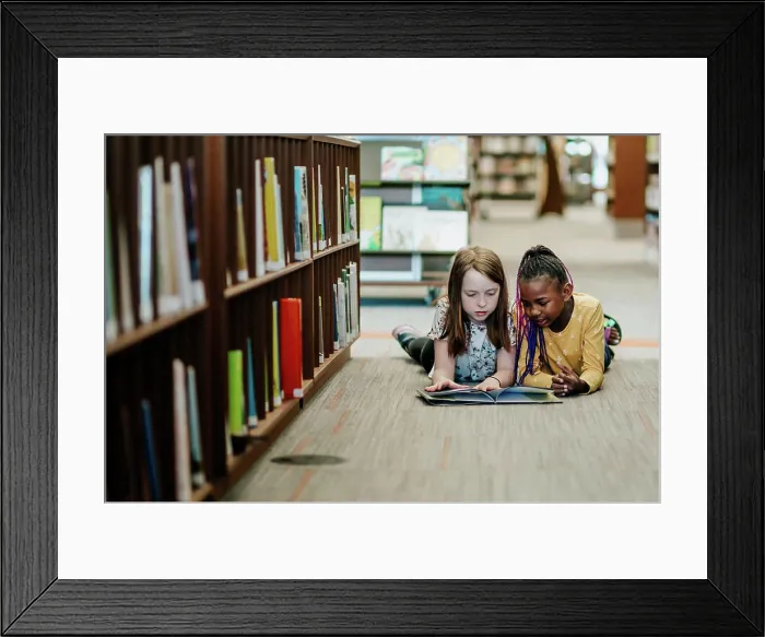 Framed Print : Two young girls reading a book on the floor of library Framed Print : Two young girls reading a book on the floor of library