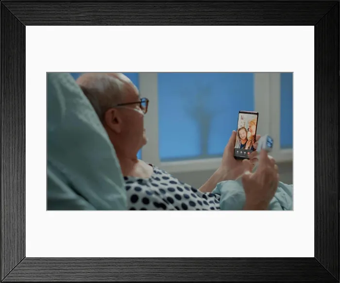 Framed Print : Sick elder patient talking on videocall with family in hospital ward