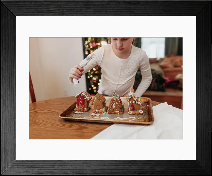 Framed Print : Young girl decorates gingerbread houses at kitchen table Framed Print : Young girl decorates gingerbread houses at kitchen table