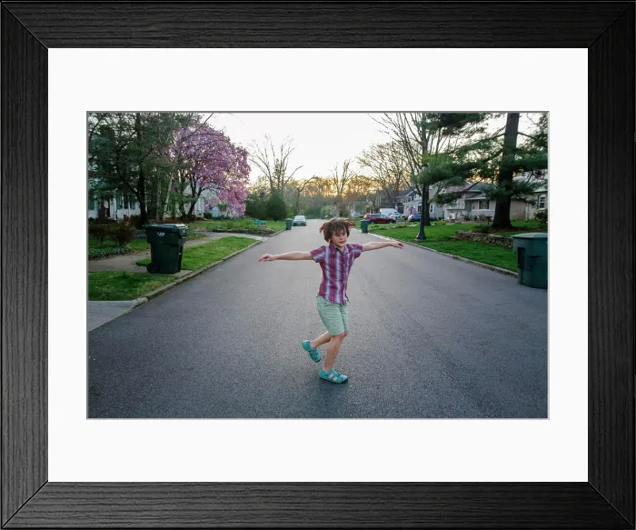 Framed Print : A happy child spins with his arms out in a street at sunset in Spring Framed Print : A happy child spins with his arms out in a street at sunset in Spring
