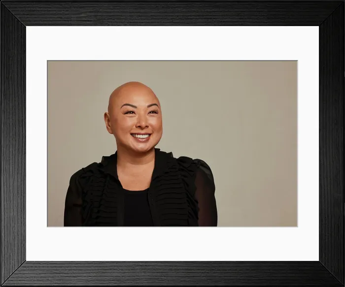 Framed Print : Stylish woman with a bald head smiling against a neutral backdrop Framed Print : Stylish woman with a bald head smiling against a neutral backdrop