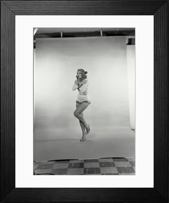 Framed Print : Vintage Photograph. A young woman in a winter outfit feeling the cold shivering with lips pursed and leg up Framed Print : Vintage Photograph. A young woman in a winter outfit feeling the cold shivering with lips pursed and leg up