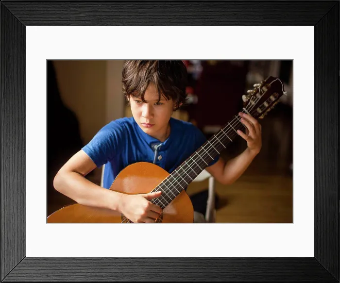 Framed Print : Close-up of a focused boy practicing classical guitar in window light Framed Print : Close-up of a focused boy practicing classical guitar in window light