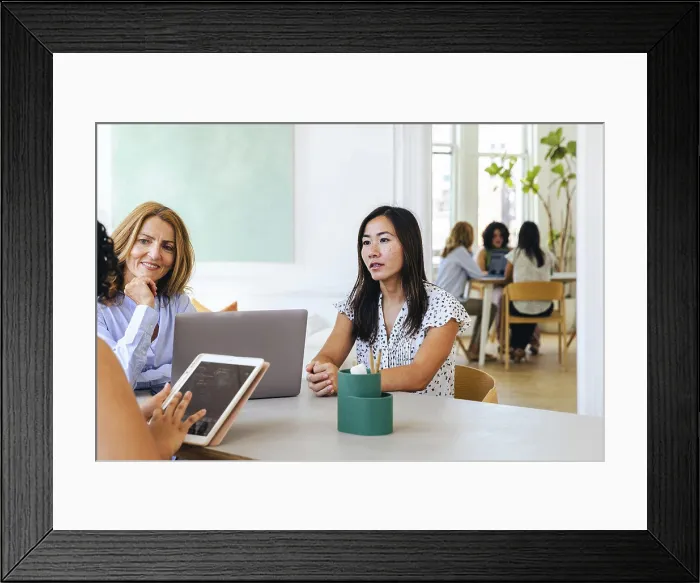 Framed Print : Businesswoman holding ipad discussing strategy with female colleagues Framed Print : Businesswoman holding ipad discussing strategy with female colleagues
