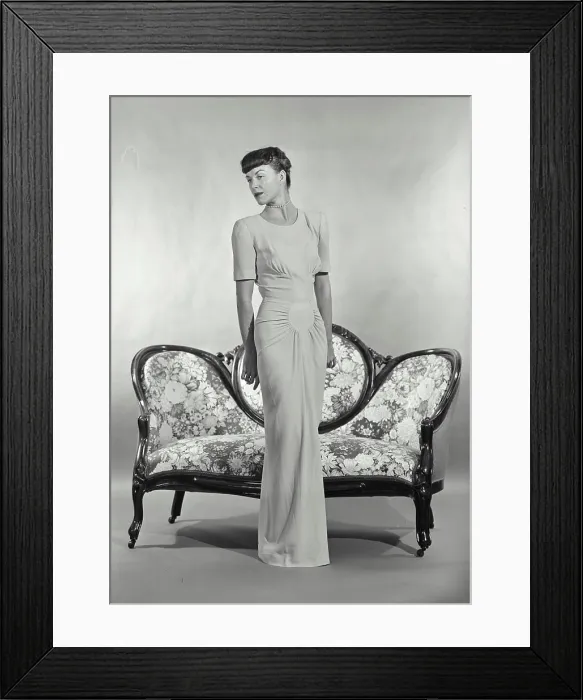 Framed Print : Vintage photograph. Woman in full length dress standing in front of small settee couch Framed Print : Vintage photograph. Woman in full length dress standing in front of small settee couch