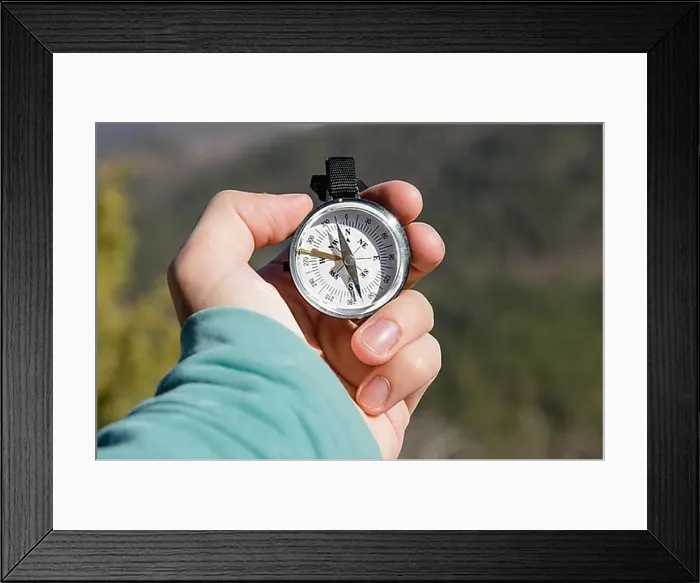 Framed Print : Close-up A man's hand holds a pocket compass against the backdrop of mountains and woods Framed Print : Close-up A man's hand holds a pocket compass against the backdrop of mountains and woods