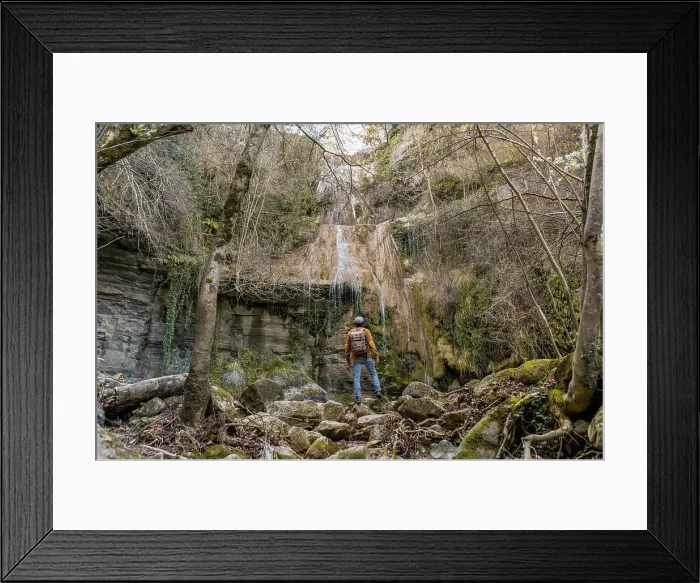Framed Print : Back view of male traveler with outstretched arms standing on stones and admiring fantastic waterfall in forest in Spain Framed Print : Back view of male traveler with outstretched arms standing on stones and admiring fantastic waterfall in forest in Spain