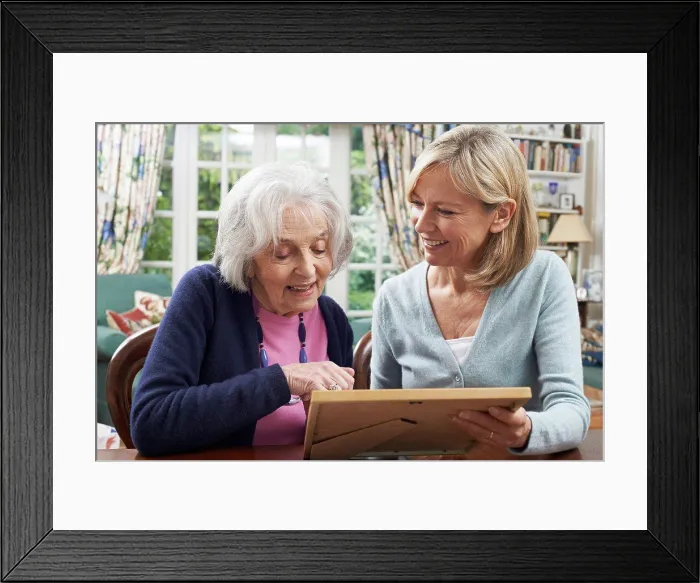 Framed Print : Senior Woman Looks At Photo In Frame With Mature Female Neighbor Framed Print : Senior Woman Looks At Photo In Frame With Mature Female Neighbor