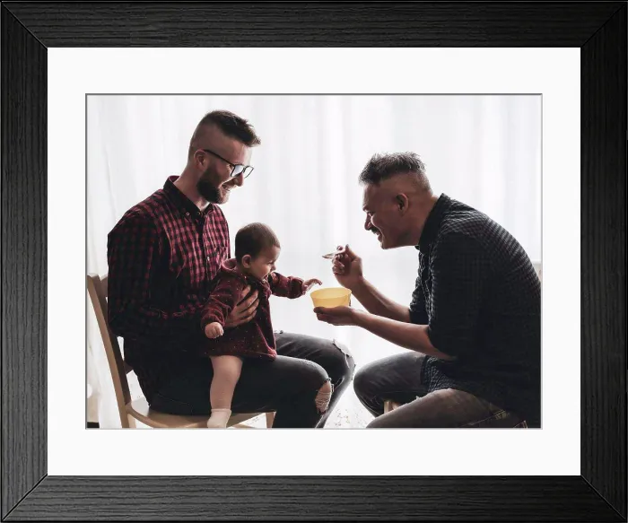 Framed Print : Male gay couple with adopted baby girl at home - Two handsome dads feed the baby girl on kitchen - Male babysitters Framed Print : Male gay couple with adopted baby girl at home - Two handsome dads feed the baby girl on kitchen - Male babysitters