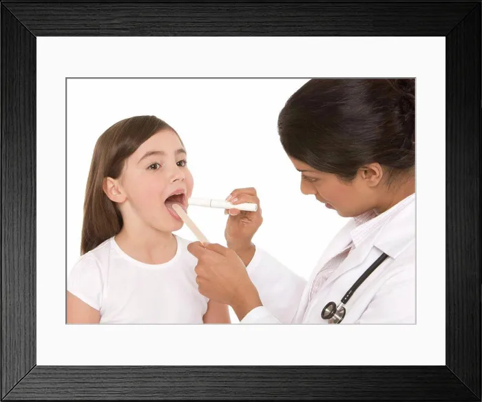 Framed Print : Throat examination. Paediatrician using a tongue depressor and a penlight to examine a girl´s throat