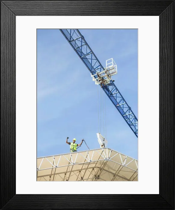 Framed Print : Low angle view of successful worker standing on roof at construction site Framed Print : Low angle view of successful worker standing on roof at construction site