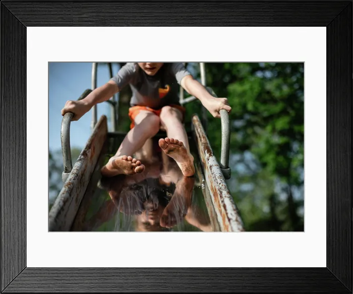 Framed Print : Child's dirty feet sliding down slide on playground at park