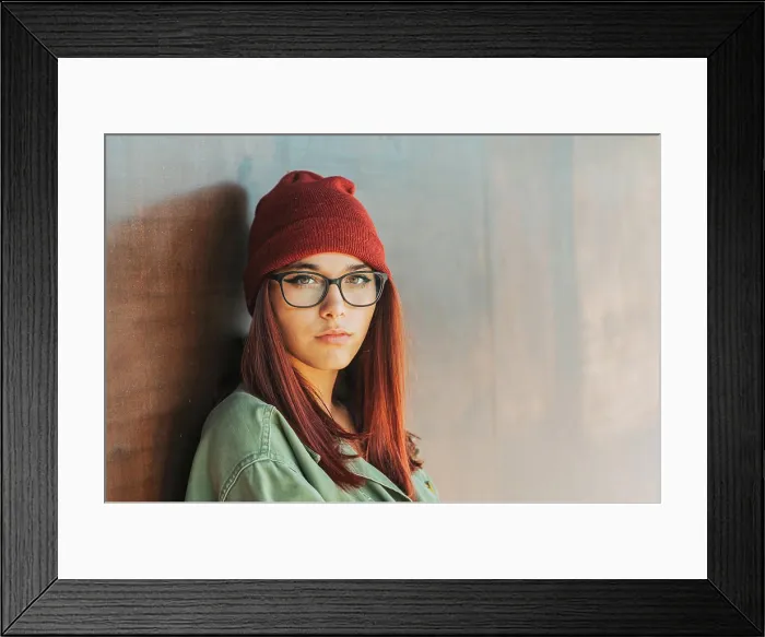 Framed Print : Thoughtful stylish woman in warm hat and glasses in dark green shirt nearby brown wall looking along
