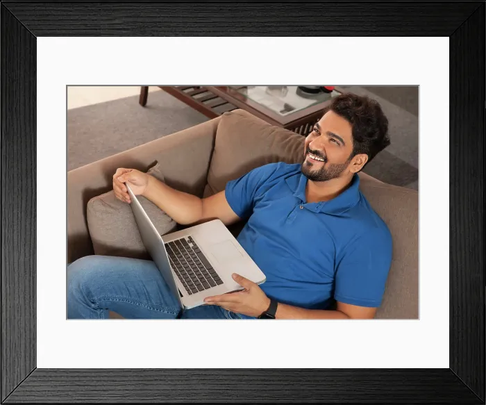 Framed Print : A happy man sitting on couch working on laptop at his home