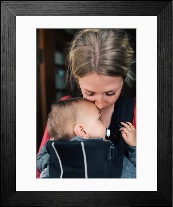 Framed Print : Loving mid adult mother carrying baby in carrier at home Framed Print : Loving mid adult mother carrying baby in carrier at home