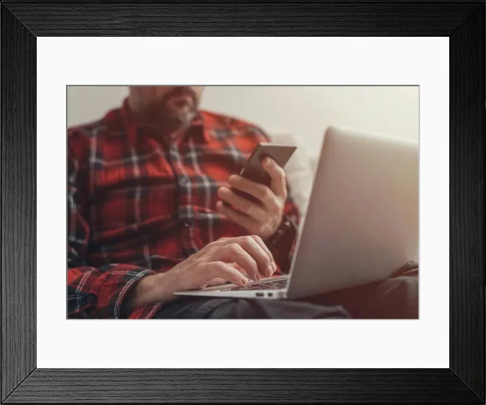 Framed Print : Man using laptop and holding smartphone Framed Print : Man using laptop and holding smartphone