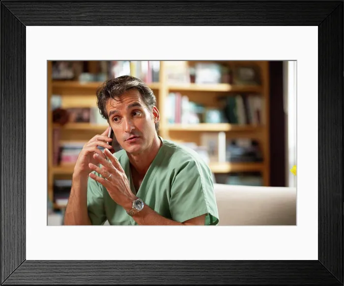 Framed Print : Hispanic Male doctor practicing tele-medicine from his home office, Talking to patient on cell phone