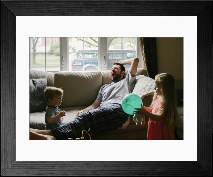 Framed Print : A tired father lies on the couch while his children play around him Framed Print : A tired father lies on the couch while his children play around him
