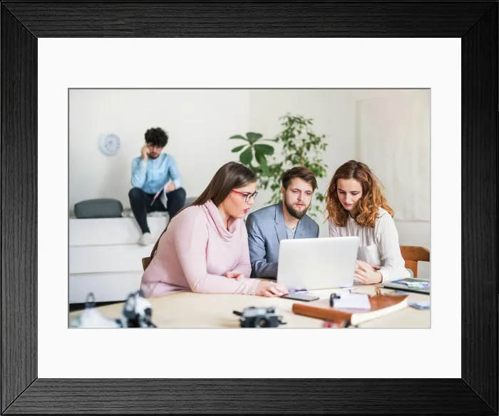 Framed Print : Young group of colleagues working on a new project together in a startup company office Framed Print : Young group of colleagues working on a new project together in a startup company office