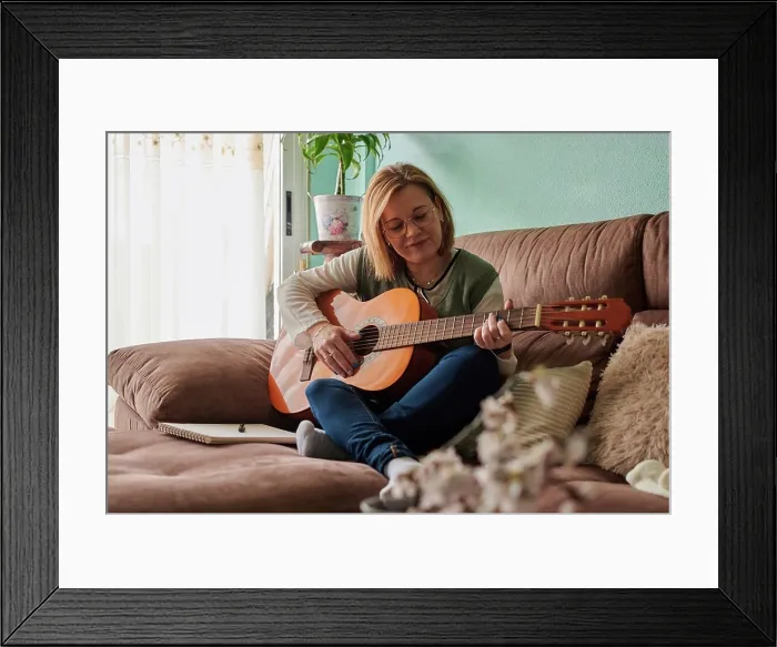 Framed Print : Middle-aged woman plays guitar on the sofa in the living room at home Framed Print : Middle-aged woman plays guitar on the sofa in the living room at home