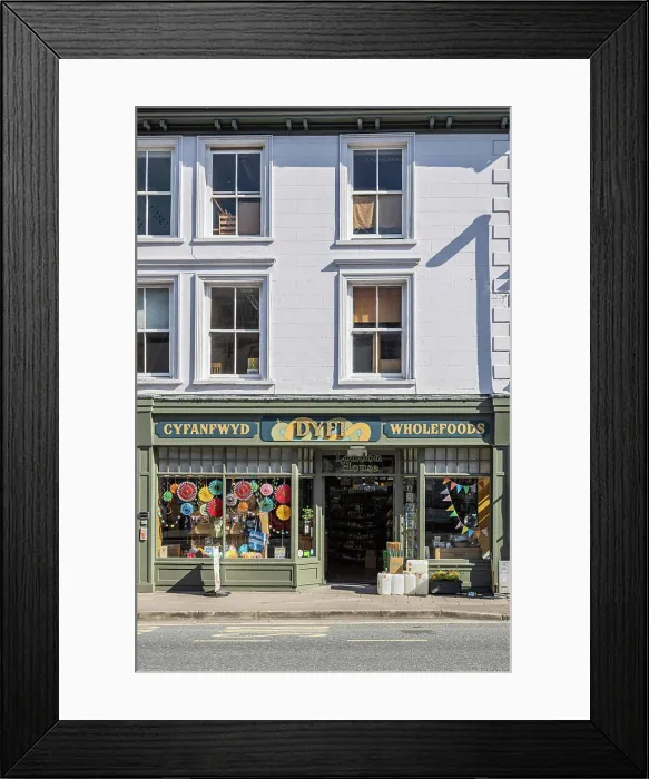 Framed Print : Machynlleth, Powys, Wales, United Kingdom. May 1, 2025. Small shop advertising Whole Foods in Welsh and English Framed Print : Machynlleth, Powys, Wales, United Kingdom. May 1, 2025. Small shop advertising Whole Foods in Welsh and English