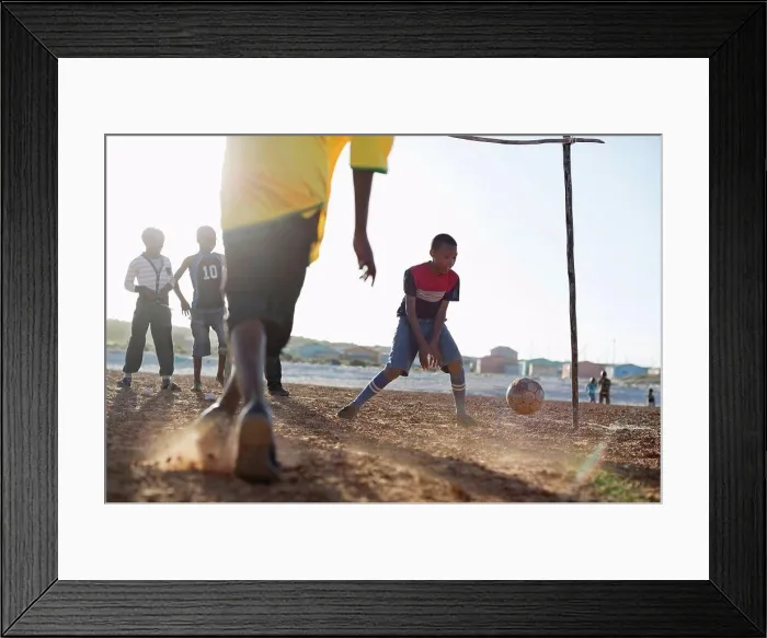 Framed Print : Boys playing soccer together in dirt field