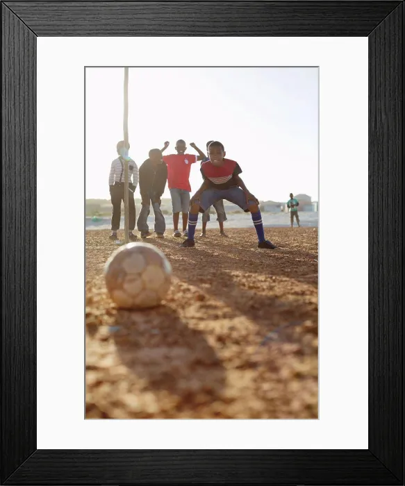 Framed Print : Boys playing soccer together in dirt field Framed Print : Boys playing soccer together in dirt field