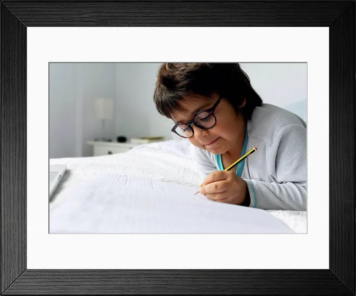 Framed Print : Portrait of little boy lying on bed doing homework Framed Print : Portrait of little boy lying on bed doing homework