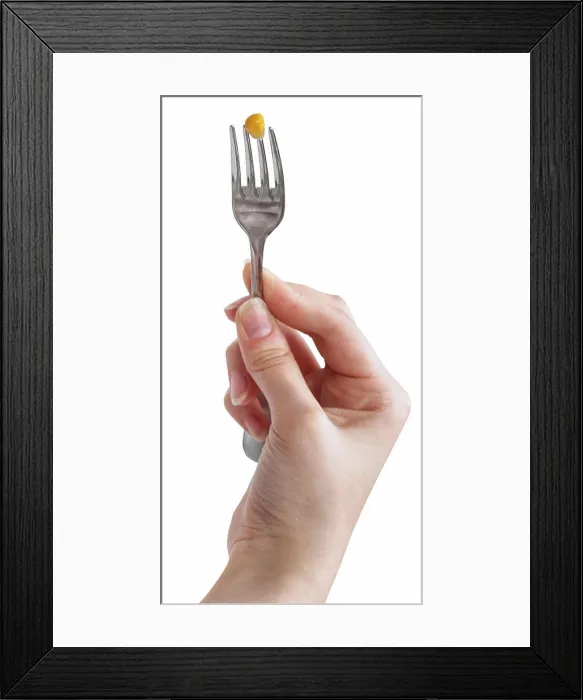 Framed Print : yellow corn seed impaled on fork in female hand one yellow corn seed impaled on fork in female hand isolated on white