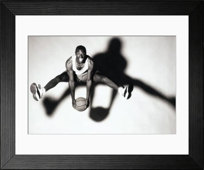 Framed Print : Portrait of a young man holding a basketball jumping up in the air