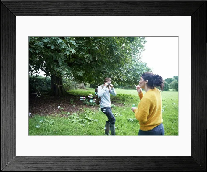 Framed Print : Couple playing with soap bubbles in field Framed Print : Couple playing with soap bubbles in field