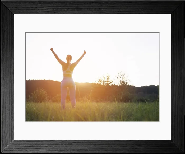 Framed Print : a girl in a fitness suit stands with her back to the camera at sunset with her hands raised after Framed Print : a girl in a fitness suit stands with her back to the camera at sunset with her hands raised after