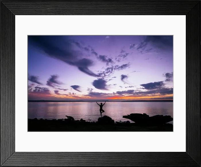 Framed Print : Silhouette of a woman performing a yoga pose on a rock by the waterside at sunset