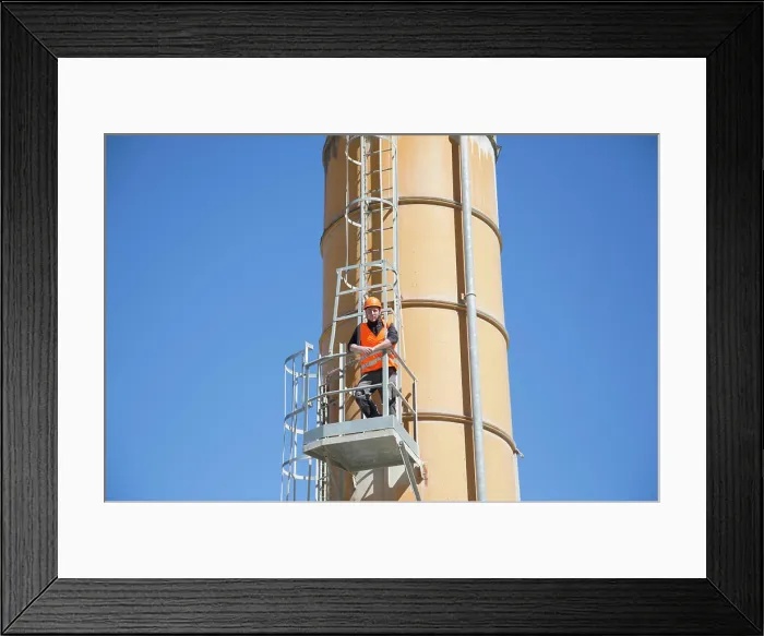 Framed Print : Worker inspecting industrial equipment against a clear blue sky Framed Print : Worker inspecting industrial equipment against a clear blue sky