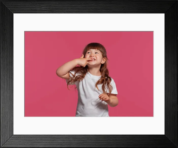 Framed Print : Close-up portrait of a little brunette girl dressed in a white t-shirt posing against a pink studio background