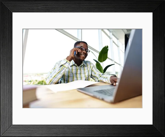 Framed Print : African man entrepreneur talking on cellphone and working on laptop at office