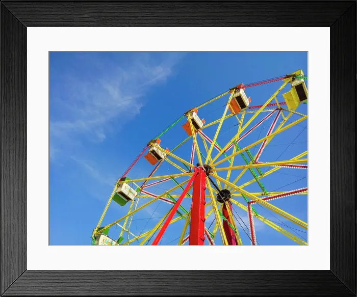 Framed Print : A ferris wheel at a funfair against a blue sky Framed Print : A ferris wheel at a funfair against a blue sky