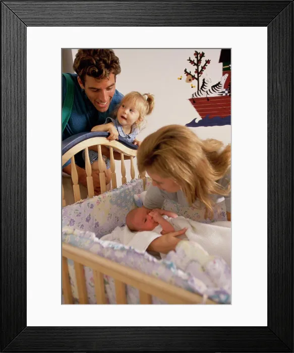 Framed Print : Father and mother looking at their baby in a crib Framed Print : Father and mother looking at their baby in a crib