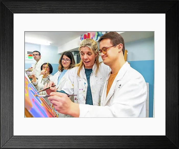 Framed Print : Instructor helping a man with down syndrome to paint on canvas in a painting class