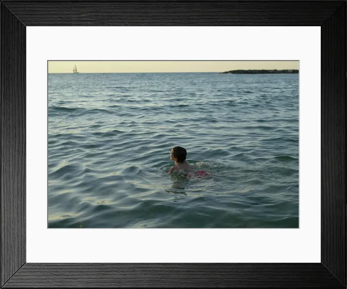 Framed Print : Child swimming in the sea at sunset with a distant sailboat on the horizon. Israel Framed Print : Child swimming in the sea at sunset with a distant sailboat on the horizon. Israel