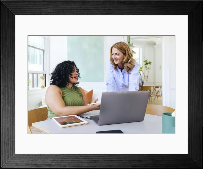 Framed Print : Creative businesswoman explaining smiling colleague over laptop Framed Print : Creative businesswoman explaining smiling colleague over laptop